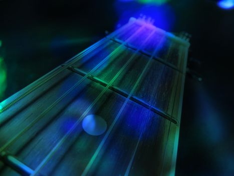 An abstract background of an acoustic guitar in green and blue concert lights.                               