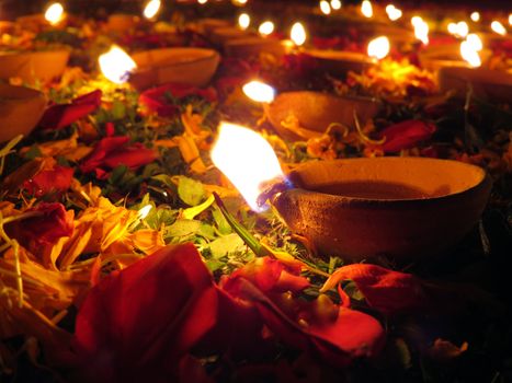 Traditional earthen oil lamps lit with flowers and petals for a holy ritual during Diwali festival in India.                               