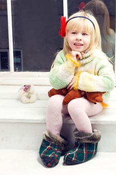 blonde little girl in knitted sweater sitting on the window