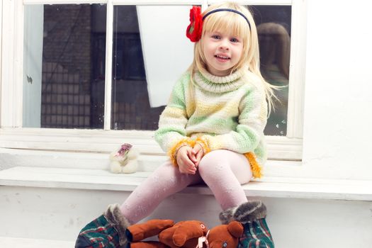 blonde little girl in knitted sweater sitting on the window