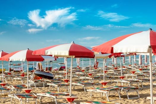 red and white umbrellas and sunlongers on the sandy beach in Italy