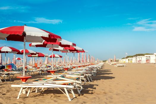 red and white umbrellas and sunlongers on the sandy beach in Italy