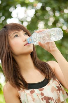 Beautiful asian girl drinking water from bottle in the park