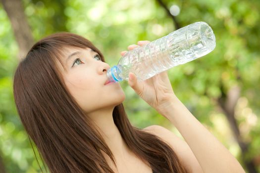 Beautiful asian girl drinking water from bottle in the park