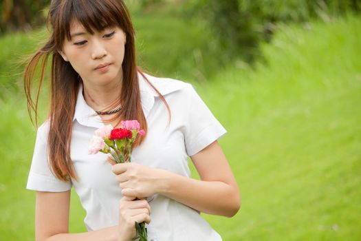 Beautiful young Thai girl holding pink carnation flower and thinking of someone