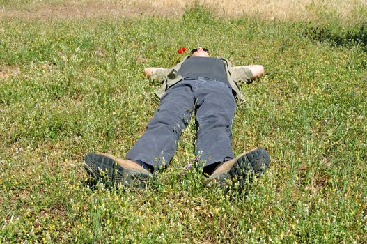 Man enjoying the sunshine. Sunbathing in green field with blooming spring flowers.