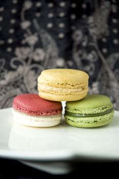 three color macarons on white plate in black background