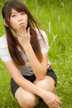Beautiful young healthy Thai girl blowing kiss in the green grass field