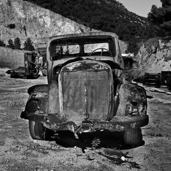 Rusty abandoned car and industrial machinery at a quarry. Black and white.