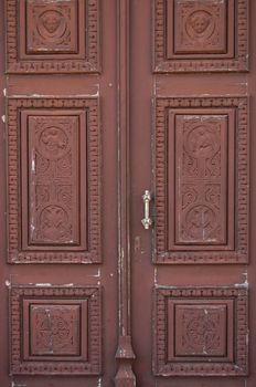 Wooden church door with carved religious symbols. Angels and cross motif.