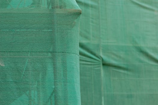 Scaffold under green debris netting at construction site. Abstract background.