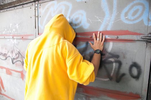 Young man in hooded sweatshirt / jumper facing grunge graffiti wall. Conceptual
