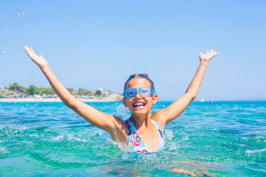 Young girl in swimming goggles playing in the wave with spray