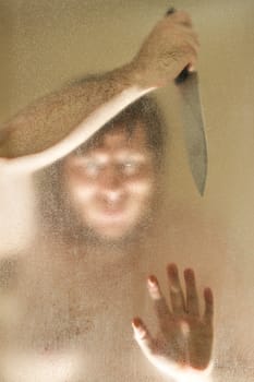 Man with a knife up against a shower door. Man's face is obscured mostly by the shower door