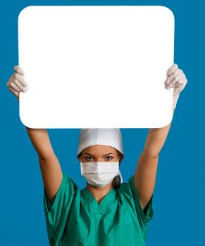 A young woman doctor in a mask holding an empty bill board over her head against a blue background.
