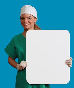 A smiling young woman doctor holding an empty white bill board against a blue background.