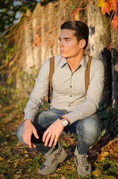 Portrait of attractive guy outdoors during fall, at sunset, in front of wooden fence
