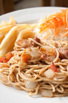 Black pepper and bacon spaghetti in plate with french fries and vegetable salad, shallow depth of field