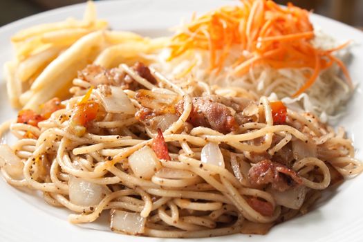 Black pepper and bacon spaghetti in plate with french fries and vegetable salad, shallow depth of field