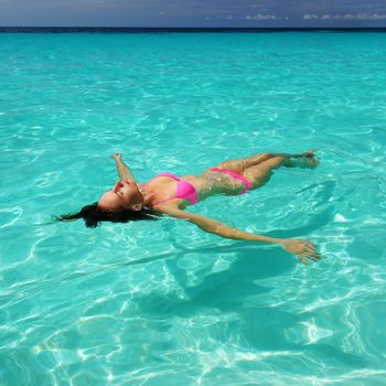 Woman in bikini lying on water at tropical beach