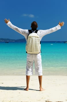 Man with backpack at tropical beach with outstretched arms