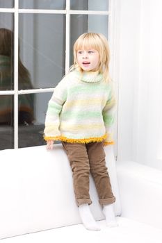 Little girl 3 years old sitting on a white couch near the window