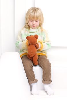 Little girl 3 years old sitting on a white couch near the window