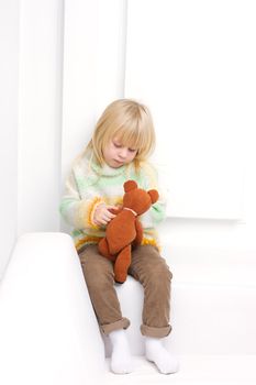 Little Girl 3 years with a brown teddy bear sitting on a white sofa