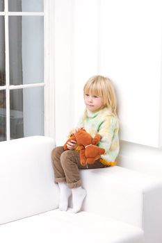 Little Girl 3 years with a brown teddy bear sitting on a white sofa