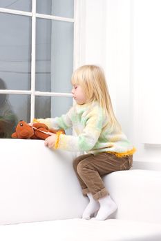 Little Girl 3 years with a brown teddy bear sitting on a white sofa