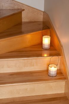 Cozy lanterns with candles decorating wooden staircase.