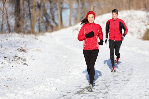 Winter running exercise couple. Runners jogging in snow. Young asian woman fitness model and caucasian man.