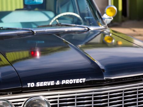 Vintage police car with detail focus on hood and reflections of warning lights in paint