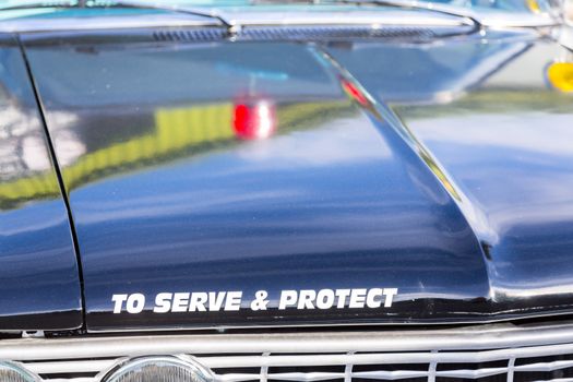 Vintage police car with detail focus on hood and reflections of warning lights in paint