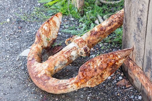 Large metal rusty anchor and rope by side of road on harbor