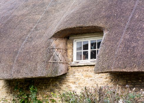 White painted wooden window under thatched roof of rural cottage