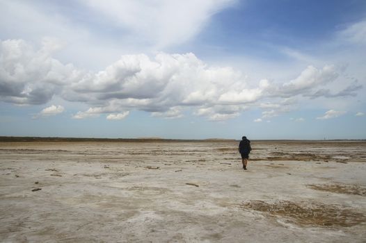 Man with backpack walking among waste landscape, salty lake Baskunckhak in summer