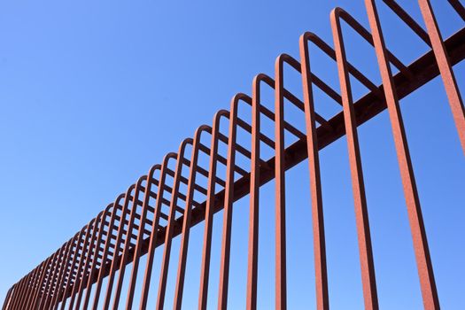 Fragment of fence with bent metal rods against a blue sky