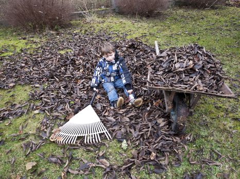 Young boy taking a break from raking leaves in the garden