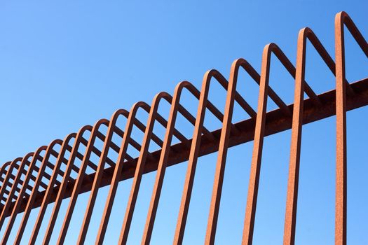 Detail of fence with bent metal rods against a blue sky
