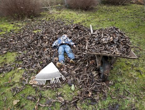 Young boy taking a break from raking leaves in the garden