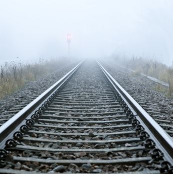 Railroad track in mist and a red signal