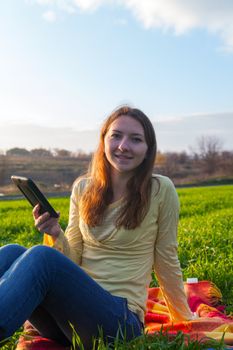 Teen girl reading electronic book sitting outdoors