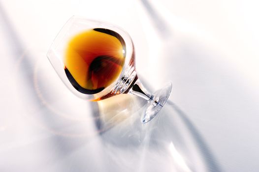 Rich brown aged cognac in an elegant tilted snifter glowing in the light against a white background conceptual of wealth and luxury