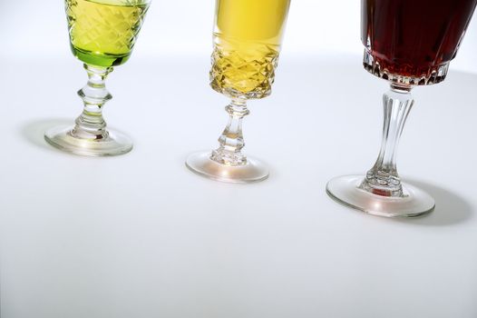 Low angle crop on white background of three cut glass wine glasses, filled with a selection of white and red wines