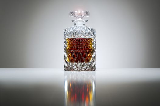 Luxury stoppered cut crystal decanter filled with whiskey or brandy on a graduated grey background with highlight and reflection