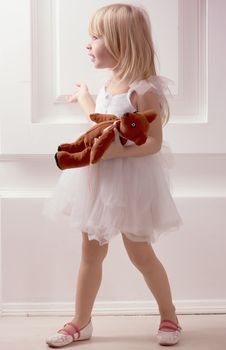 3 years old girl in a white dress with a toy against the wall