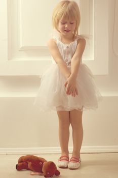 3 years old girl in a white dress with a toy against the wall