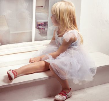Girl 3 years old in a beautiful white dress near the winter window