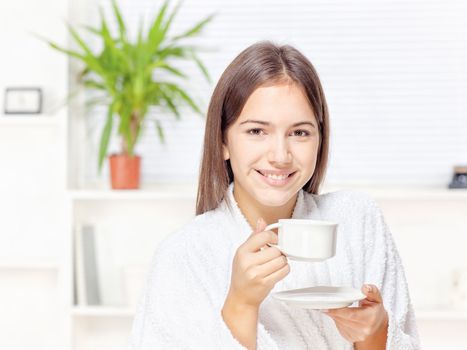 Woman in bathrobe holding cup at home